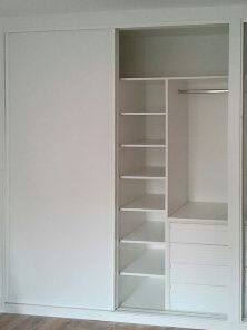 Un armario blanco con puertas correderas y estantes en un dormitorio.