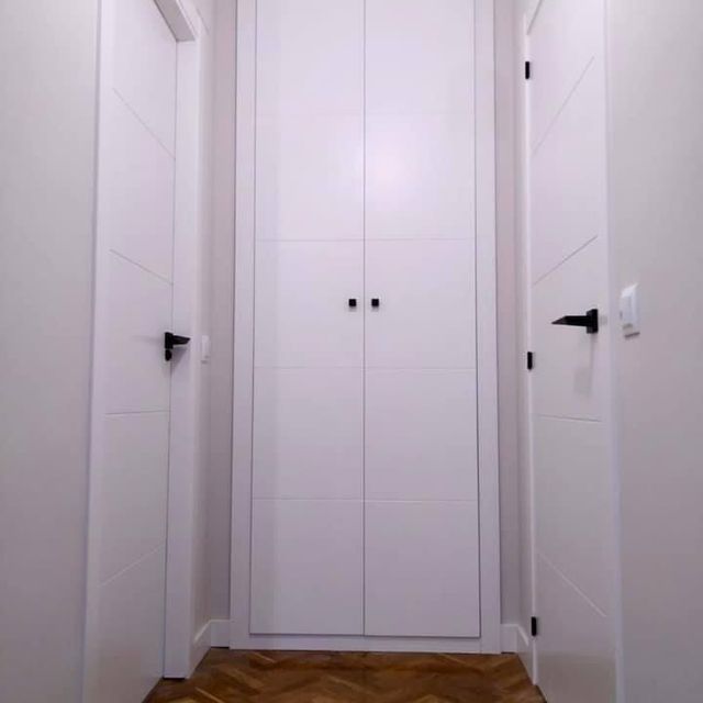 Un pasillo con dos puertas blancas y suelo de madera.