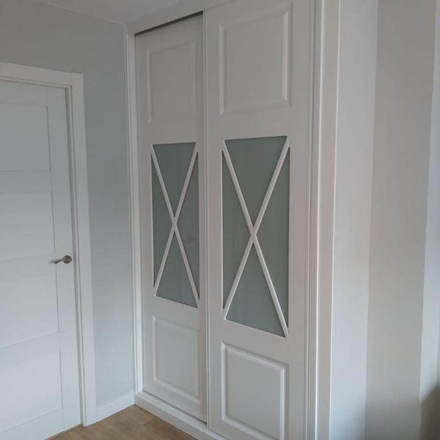 Un armario blanco con puertas corredizas de cristal en un dormitorio.