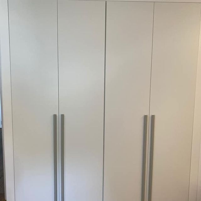 En una habitación hay un armario blanco con tiradores plateados.