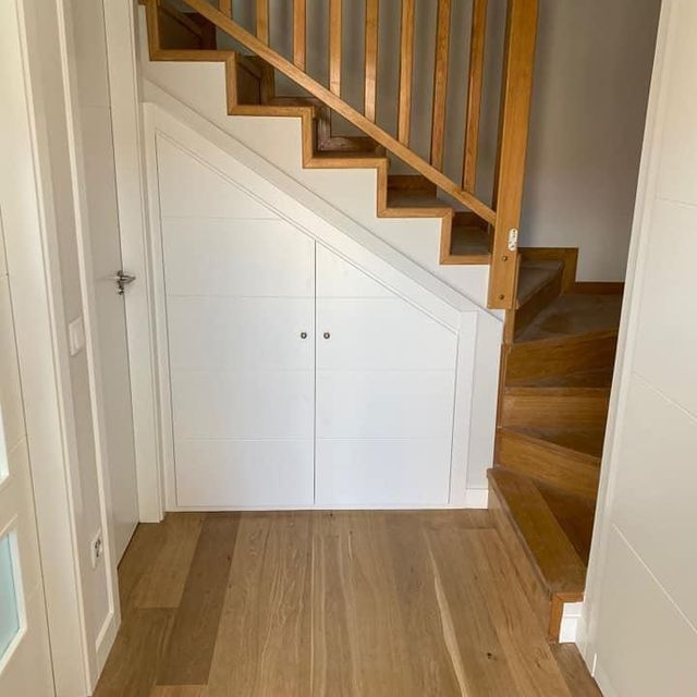 Un pasillo con escaleras de madera y un armario blanco debajo de ellas.