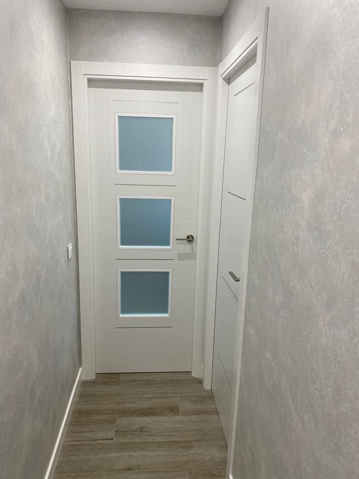 Un pasillo con una puerta blanca y suelo de madera.