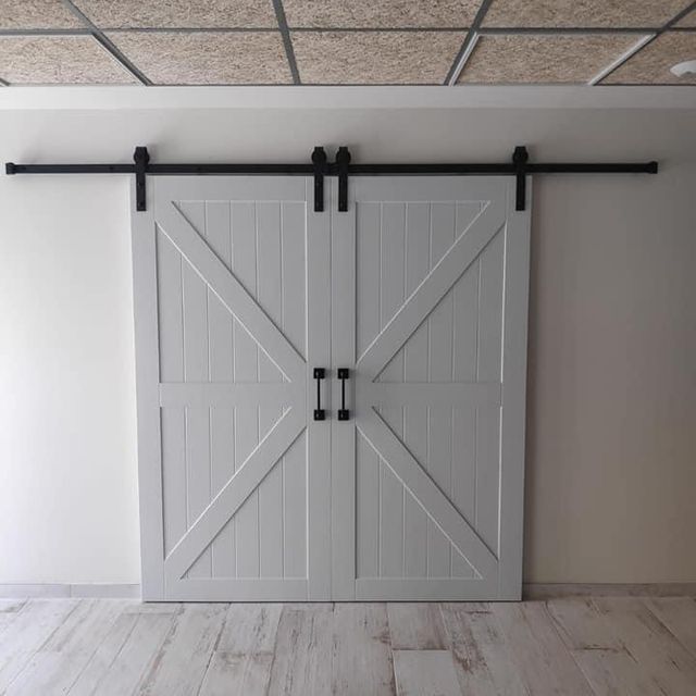 Una puerta de granero corrediza blanca está colgada en una pared blanca.