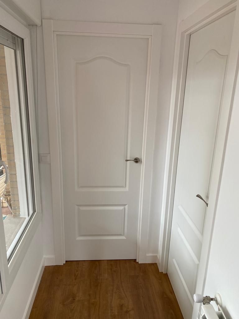 Un pasillo con una puerta blanca y una ventana.