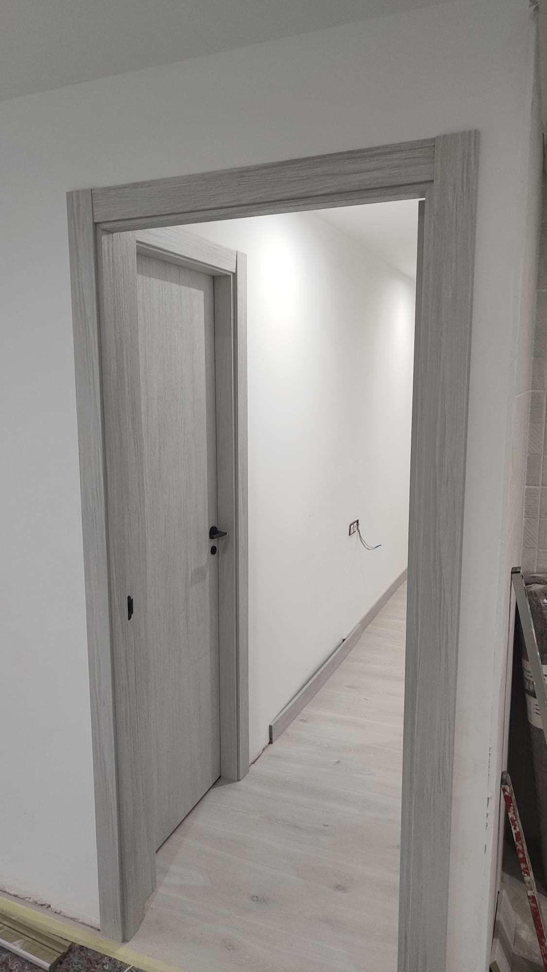 Un pasillo con una puerta y una pared blanca.