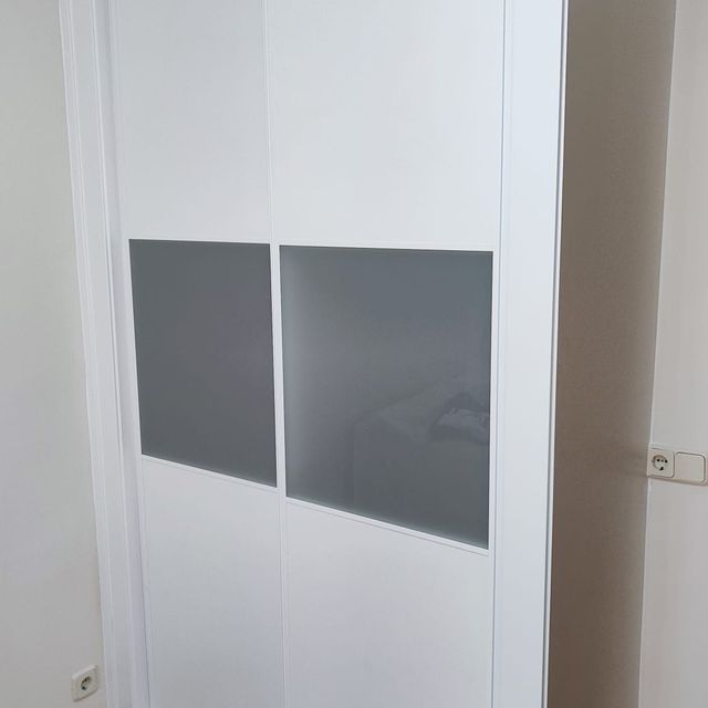 Un armario blanco con puertas corredizas de cristal en un dormitorio.