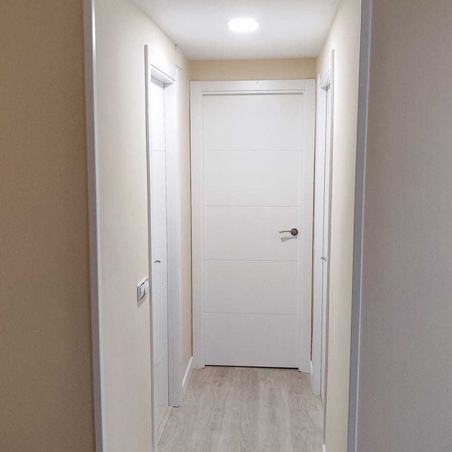 Un pasillo largo con una puerta blanca y piso de madera.