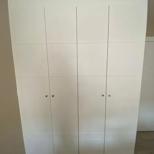 En una habitación hay un armario blanco con cuatro puertas.