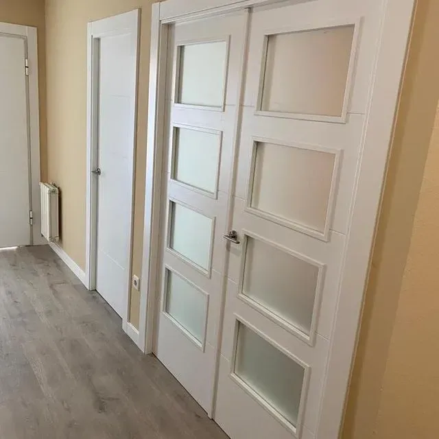 Un pasillo con una hilera de puertas blancas con vidrio esmerilado.