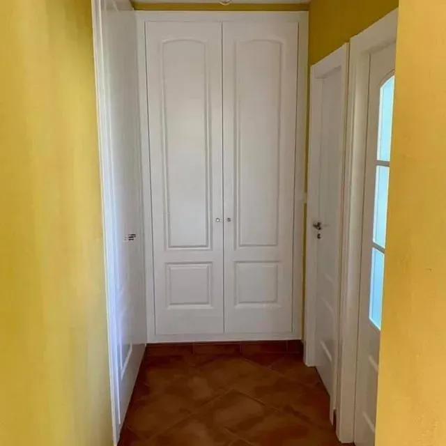 Un pasillo con paredes amarillas y armarios blancos.