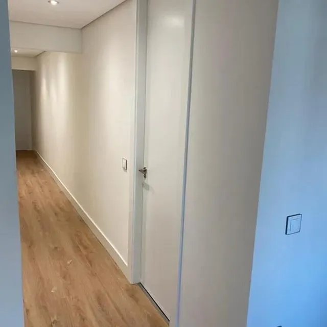 Un largo pasillo con suelos de madera y paredes blancas.