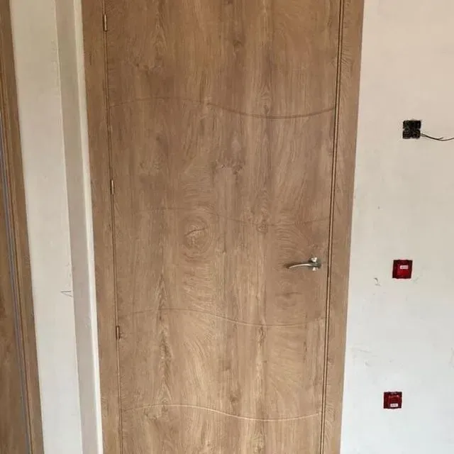 Una puerta de madera está en una habitación al lado de una pared blanca.