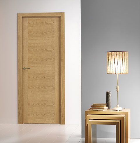 Una puerta de madera está en una habitación al lado de una lámpara y una pila de mesas de madera.