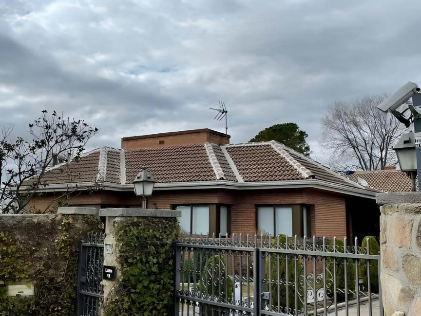 Una casa de ladrillo con techo de tejas y una valla alrededor.