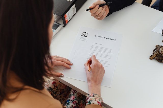 Una mujer está sentada en una mesa firmando un documento con un bolígrafo.