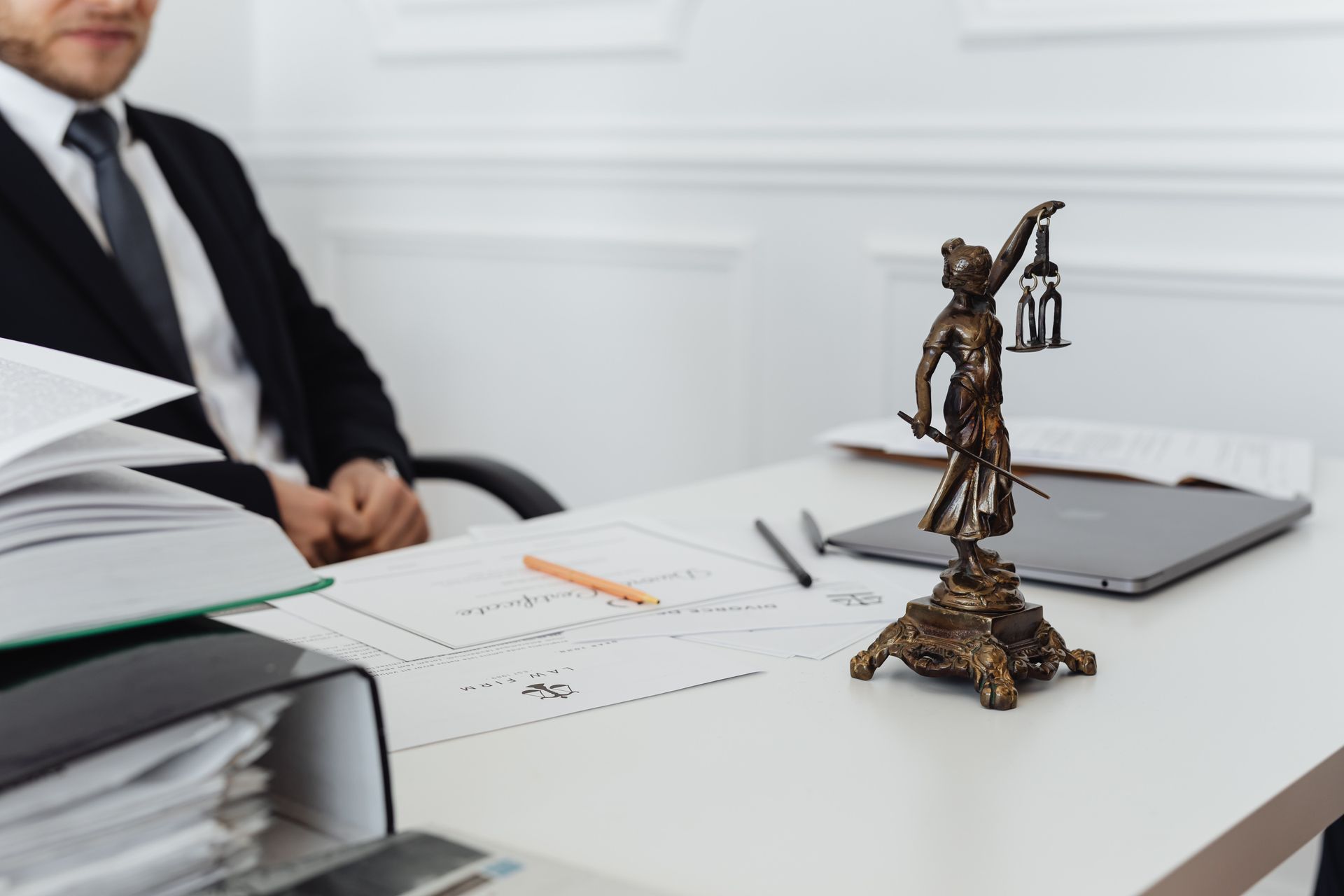 Un hombre está sentado en un escritorio con una estatua de la justicia sobre él.