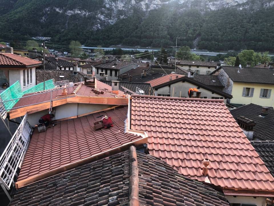 Tetti di vari edifici di una città, tegole in terracotta, con montagne sullo sfondo.