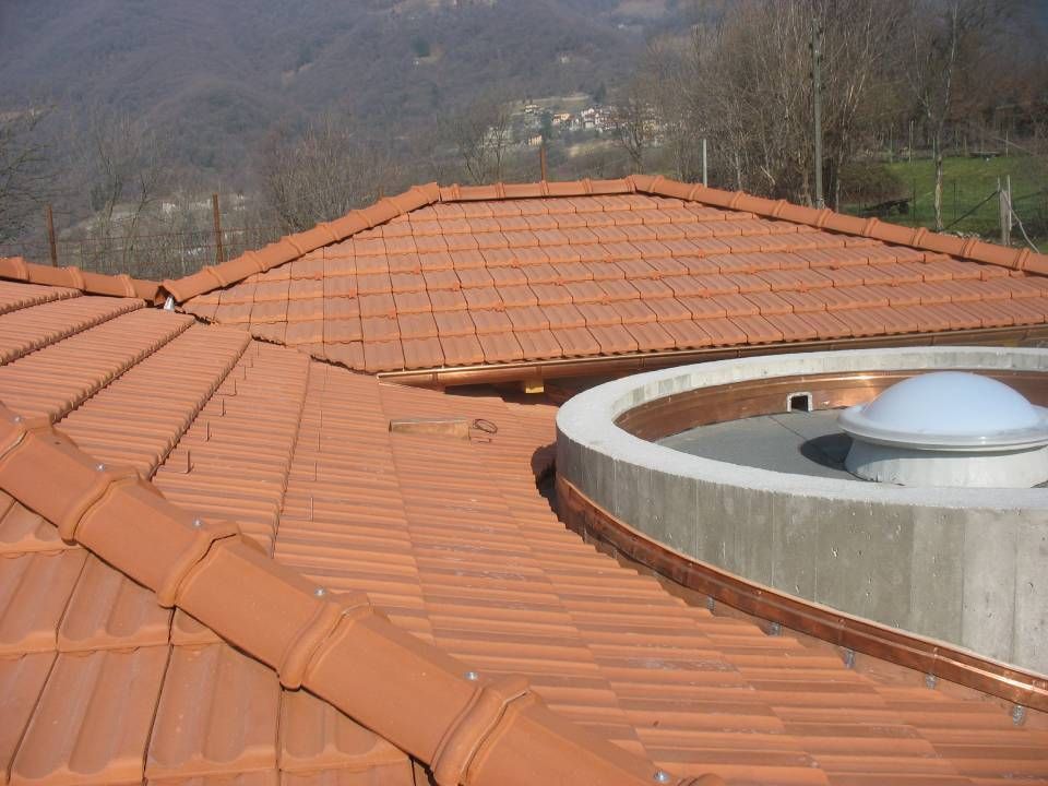 Tetto in tegole di terracotta con raccordi in rame e lucernario circolare. Sullo sfondo montagne.