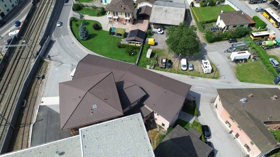 Vista aerea di un edificio con tetto marrone e del quartiere circostante con binari del treno e strada.