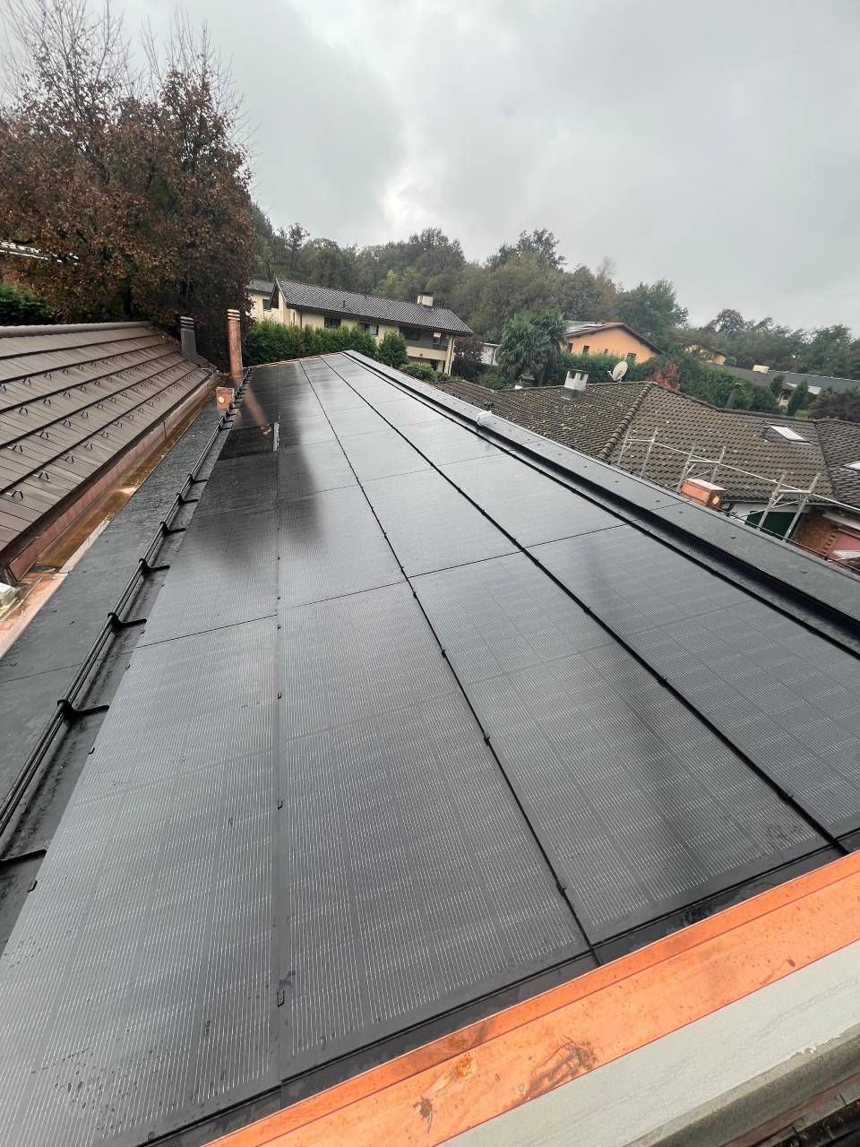 Pannelli solari neri installati su un tetto piastrellato, con vista sul quartiere in una giornata nuvolosa.