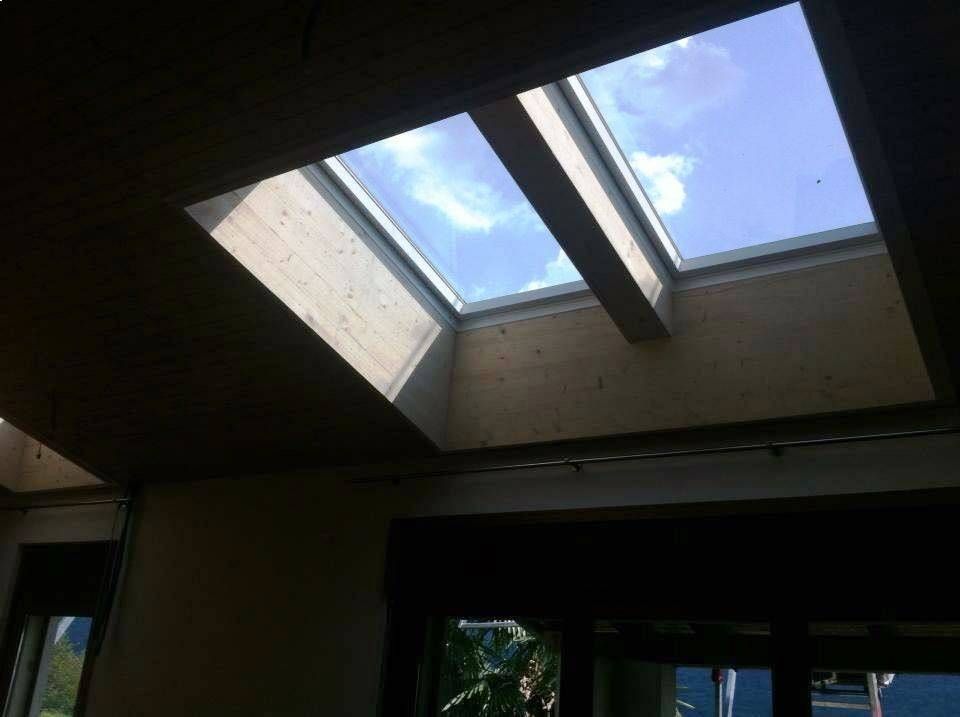 Vista interna con due lucernari che si affacciano sul cielo azzurro. Pareti beige e travi in legno incorniciano i lucernari.