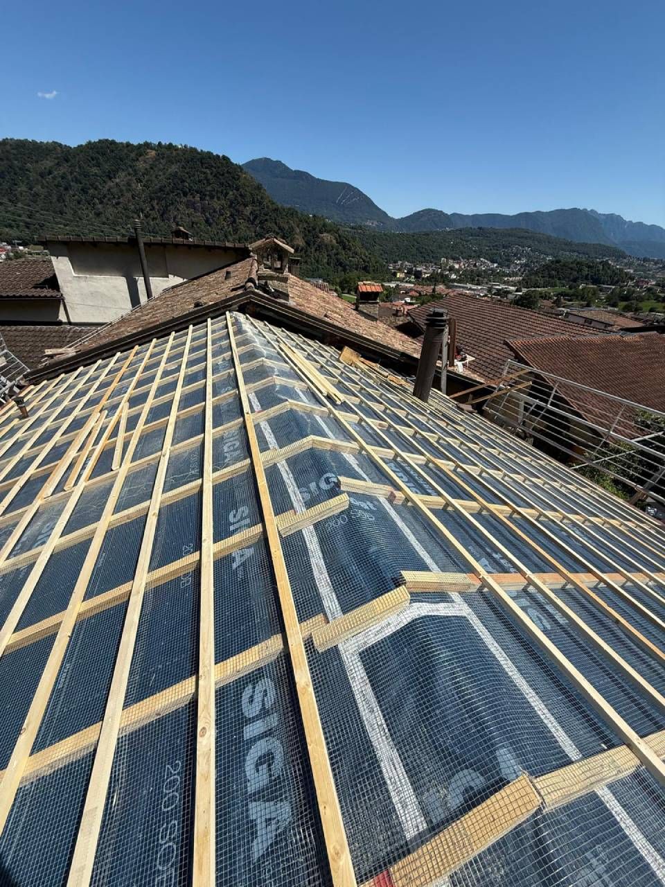 Struttura del tetto con travi in legno e sottofondo nero, sullo sfondo delle montagne.