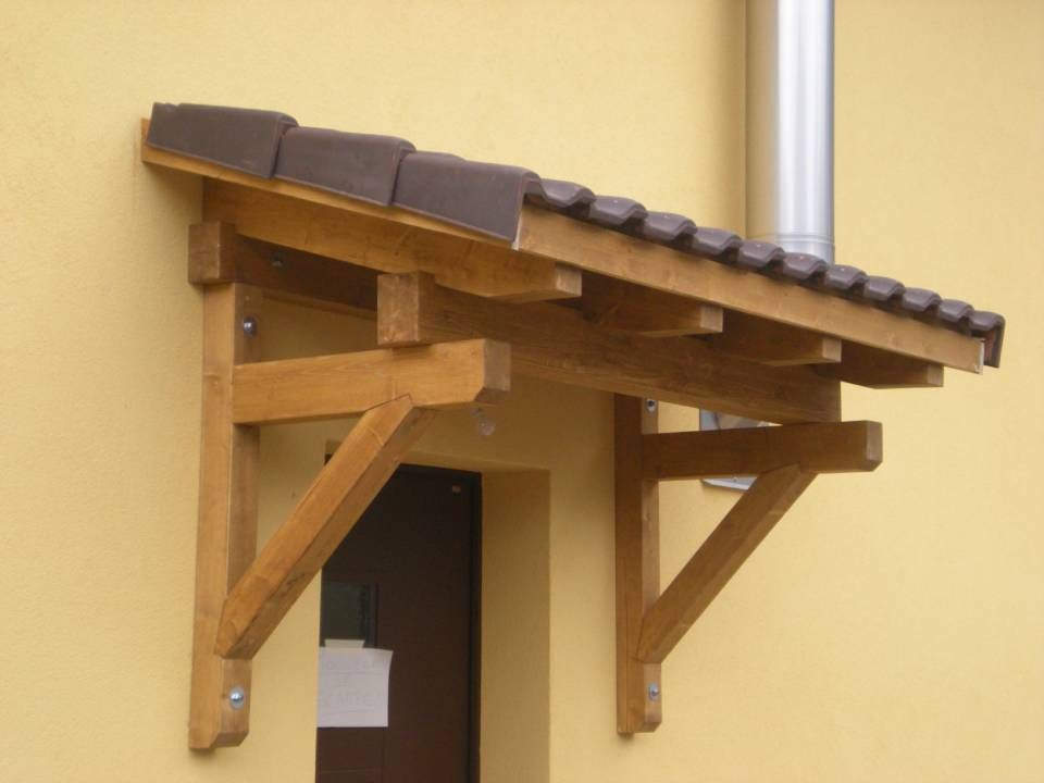 Tenda da sole in legno con tegole marroni sopra una porta, montata su una parete esterna gialla.