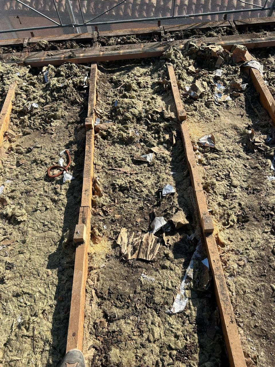 Travi di legno su un tetto ricoperto di materiale isolante, detriti e carta strappata.