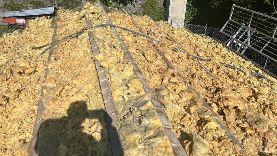 Isolamento giallo tra le travi di legno di un tetto, figura in ombra.