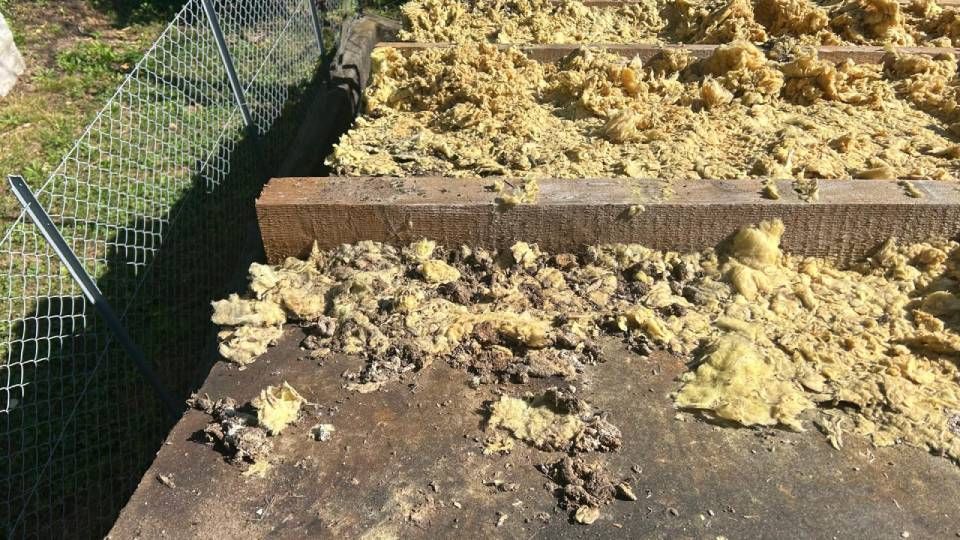 Tetto danneggiato con isolamento esposto e detriti accanto a una recinzione a maglie di catena.