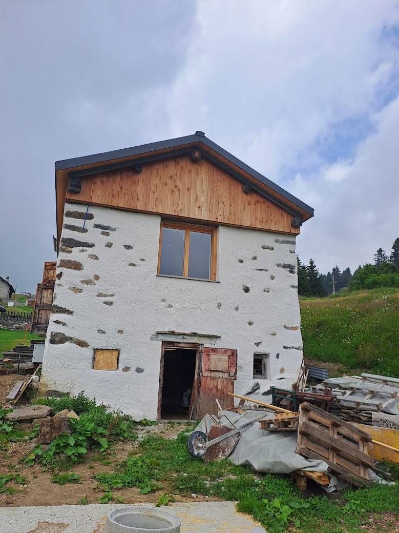 Edificio in pietra con tetto in legno e porta aperta, situato su una collina erbosa sotto un cielo nuvoloso.