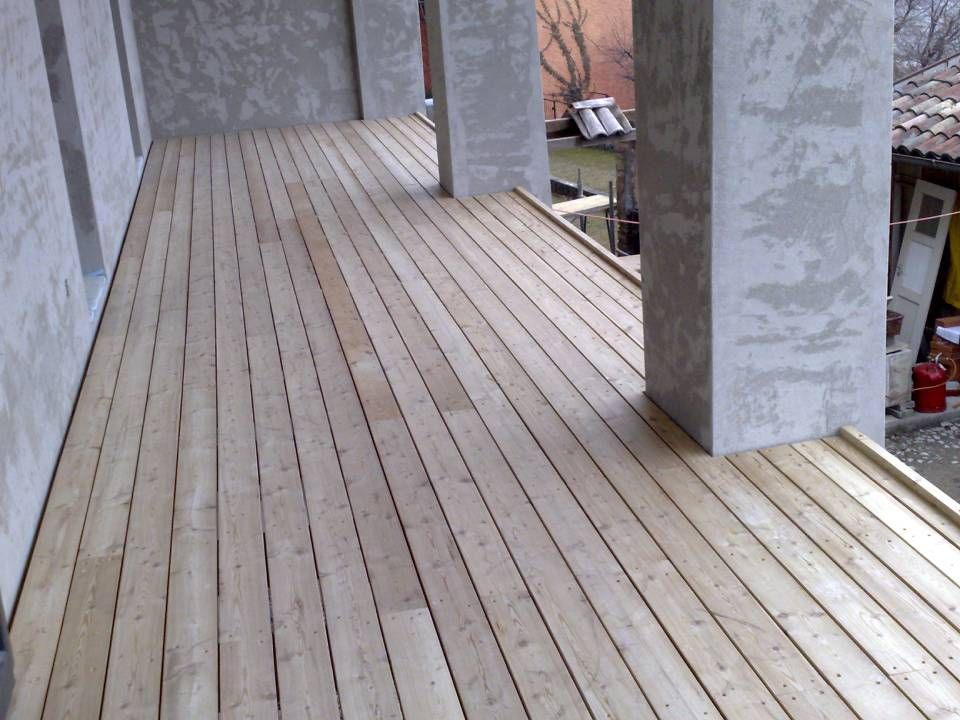 Terrazza in legno con assi verticali, pilastri e pareti in cemento, vista esterna.