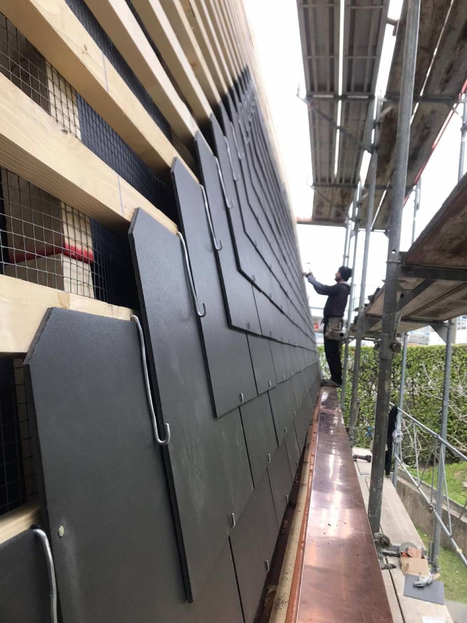 Un operaio edile installa pannelli grigio scuro sul lato di un edificio, con le impalcature in vista.