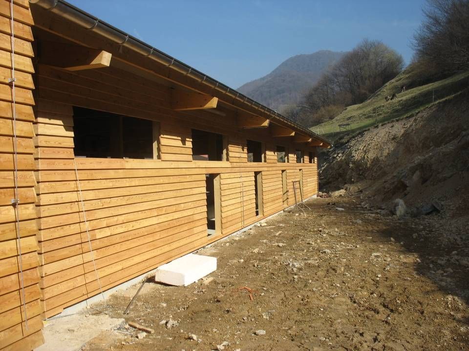 Edificio in legno in costruzione in un ambiente montano con travi a vista e terreno sterrato.