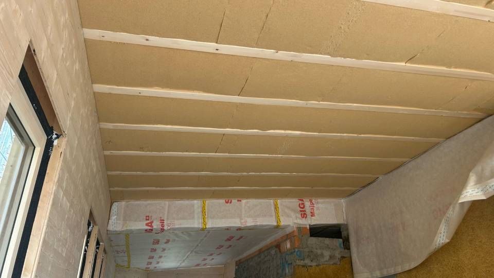 Vista interna di un soffitto con travi in ​​legno a vista e isolamento. Lavori in corso, dettagli della stanza visibili.