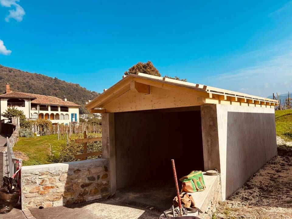 Garage in costruzione con struttura del tetto in legno, sullo sfondo case e colline sotto un cielo azzurro.