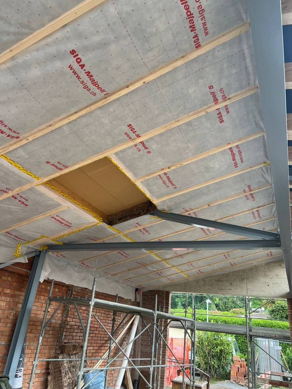 Costruzione del tetto interno, con struttura in legno, isolamento e mattoni a vista, con un'apertura.