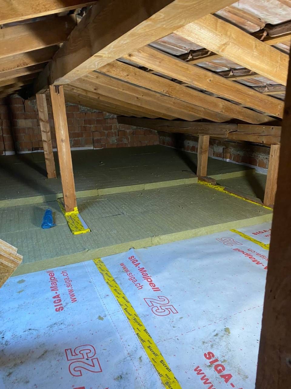 Soffitta con isolamento installato tra travi e travetti in legno. Nastro giallo sigilla la barriera al vapore.
