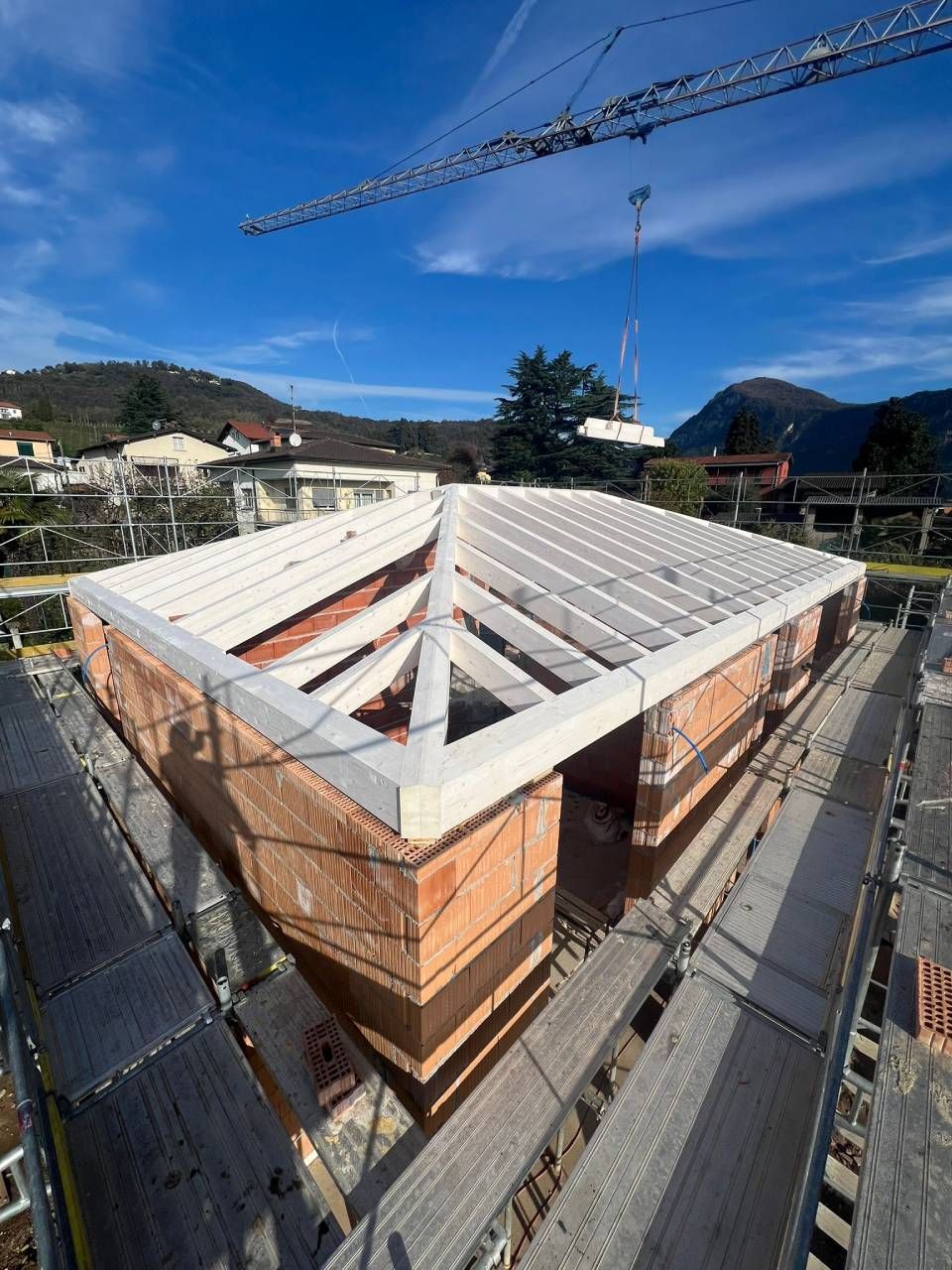 Cantiere con un edificio in mattoni in costruzione sotto un cielo azzurro, sono visibili impalcature e una gru.
