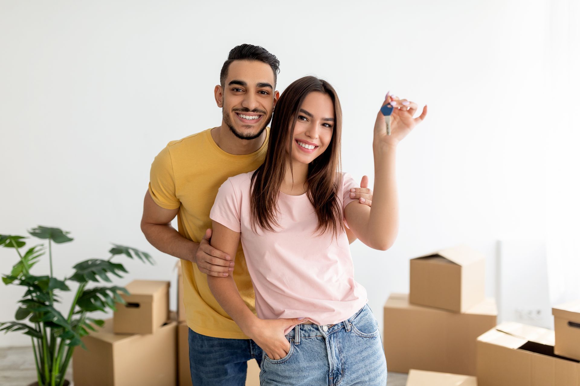 Un jeune couple avec les clefs de leur maison dans la main et des cartons dans le fond