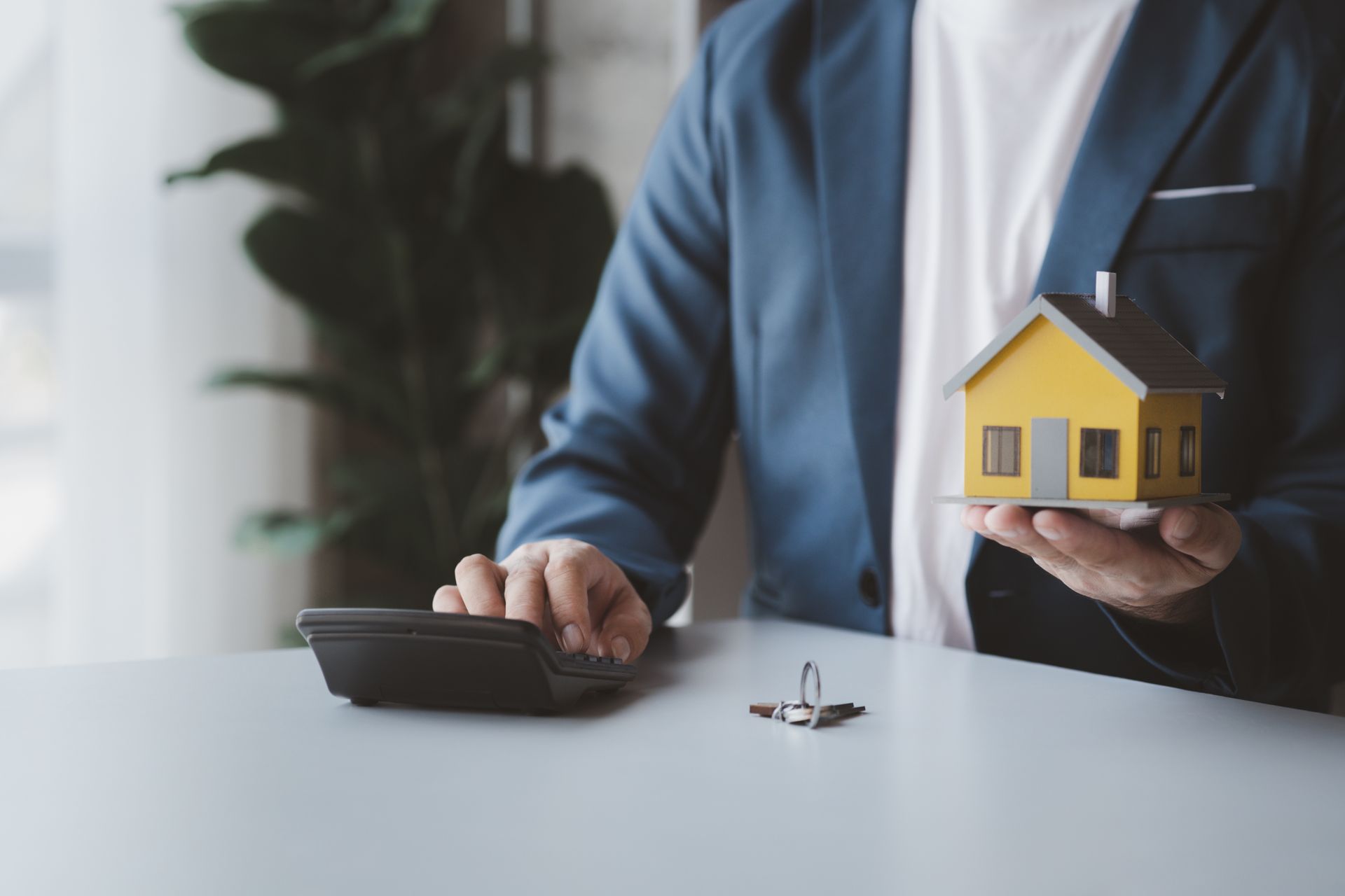 Un assureur en train de calculer une some avec une maison dans la main