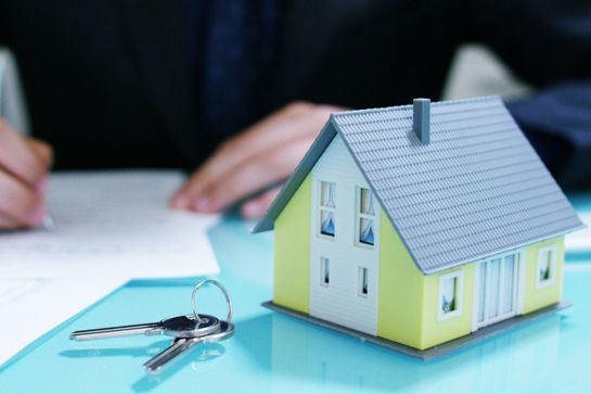 Modell eines kleinen gelben Hauses mit grauem Steildach und Schlüsselbund mit zwei Schlüsseln