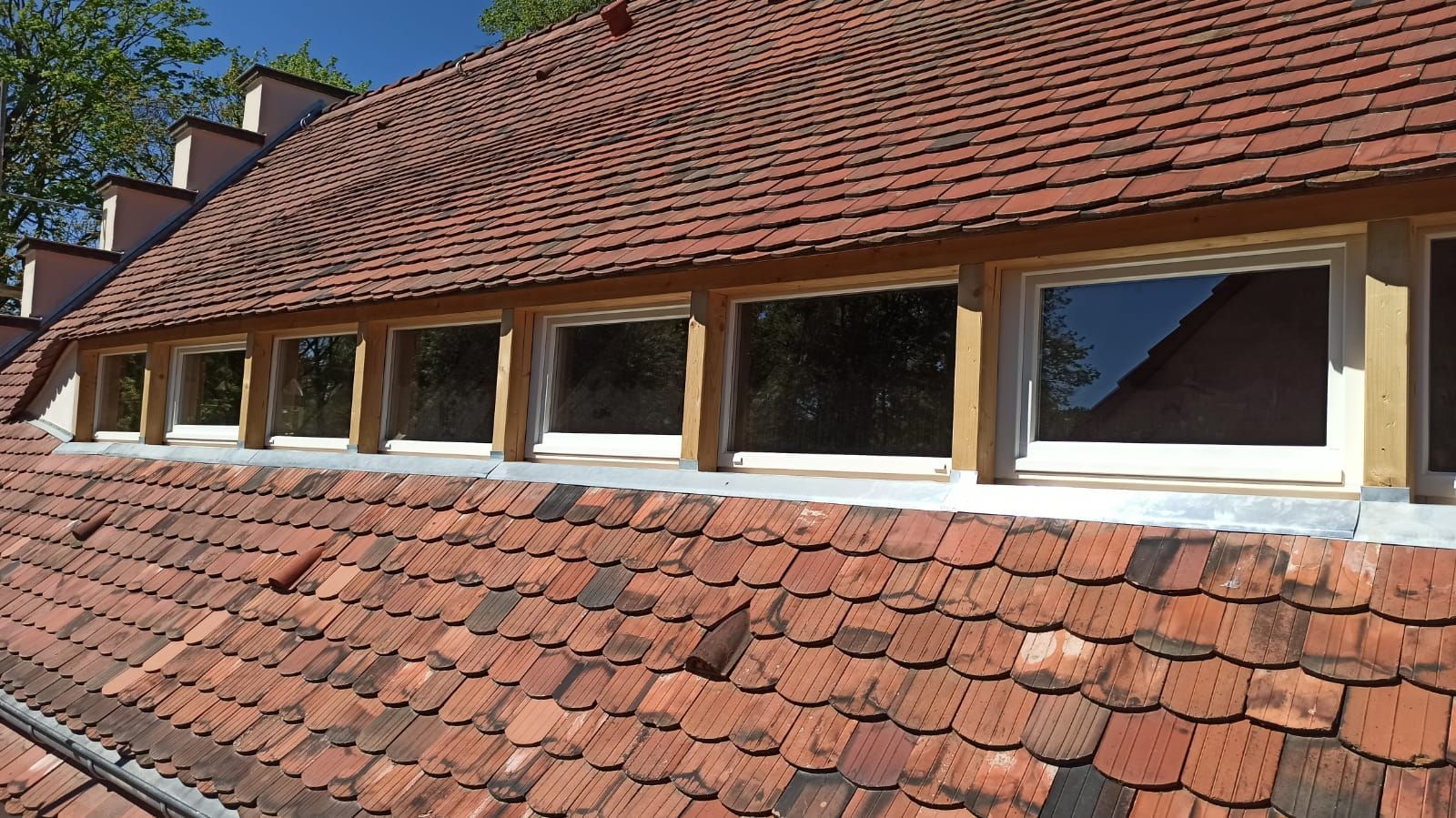 Sanierung eines roten Ziegeldachs mit mehreren rechteckigen Dachfenstern.