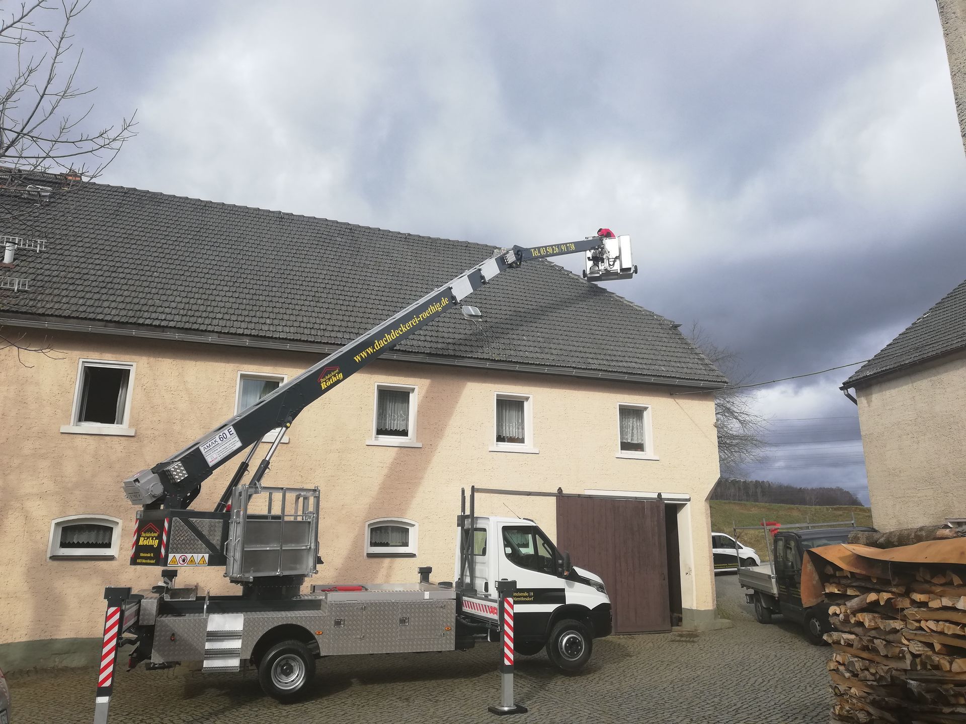 Sanierungsarbeiten an einem Steildach mit dunklen Dachziegeln und Hebebühne.