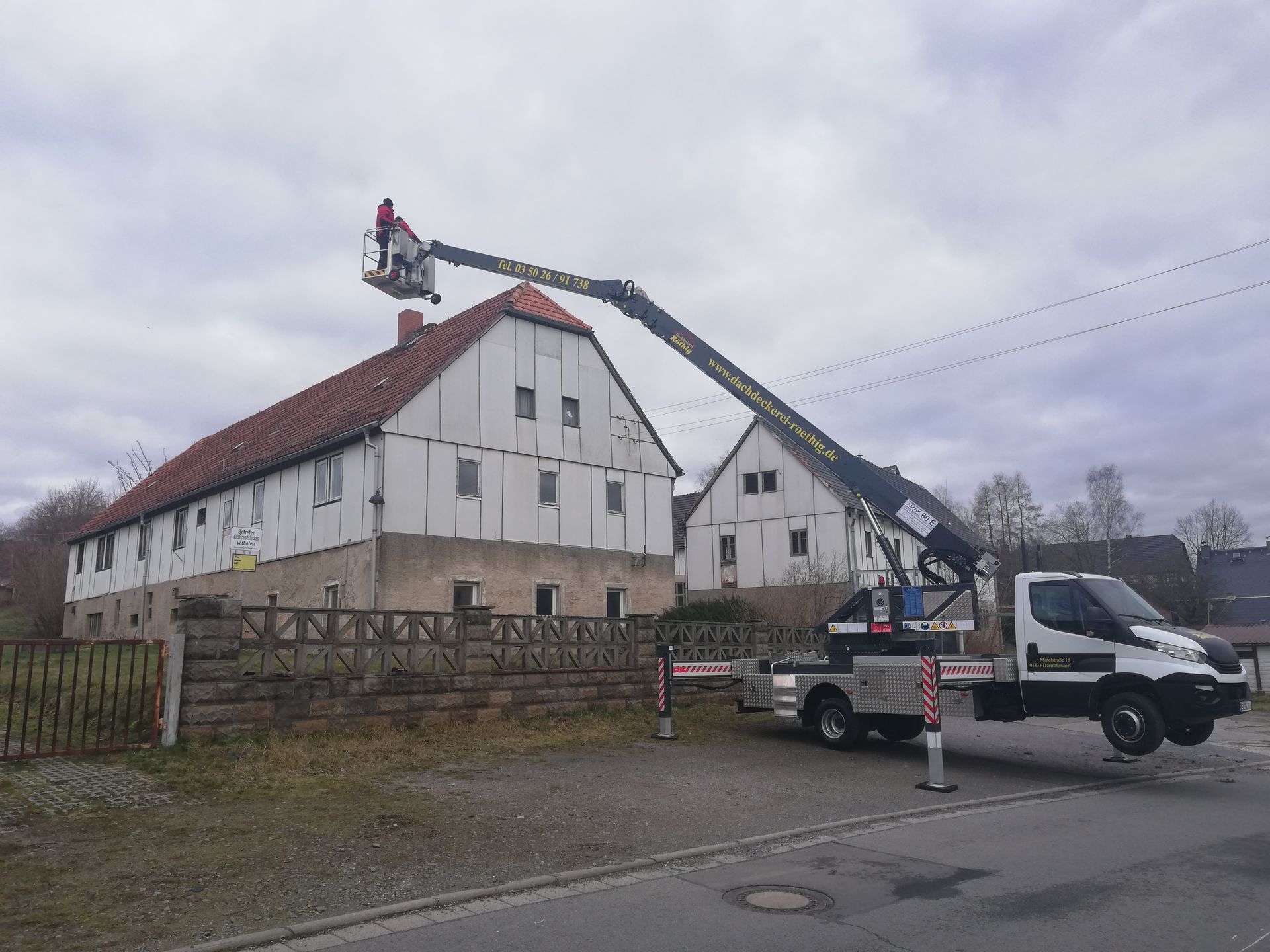 Arbeiter auf einer Hebebühne bei der Sanierung eines großen Satteldachs.