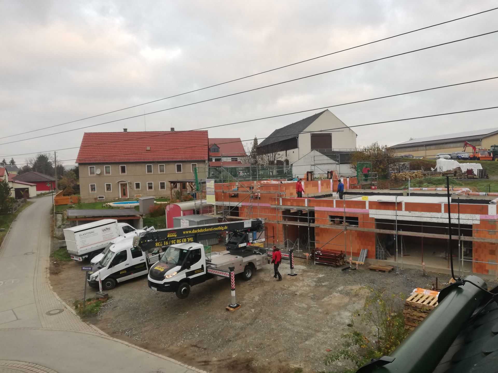 Baustelle mit mehreren Rohbauten in Ziegelbauweise und Sanierungsarbeiten am Dach im Gange.