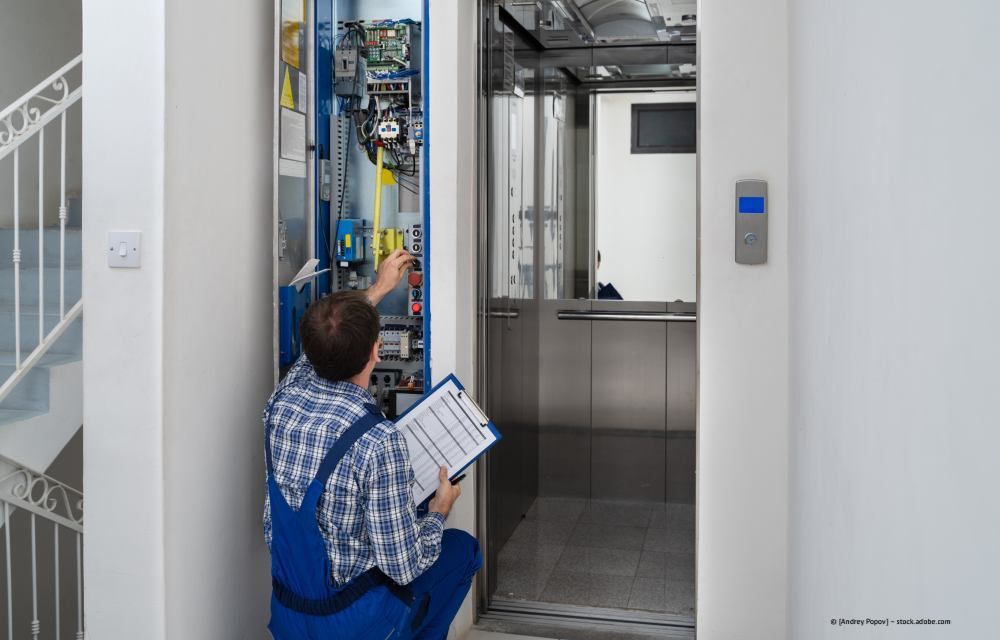 Techniker überprüft mit Klemmbrett die Aufzugssteuerung in der Eingangshalle eines Gebäudes