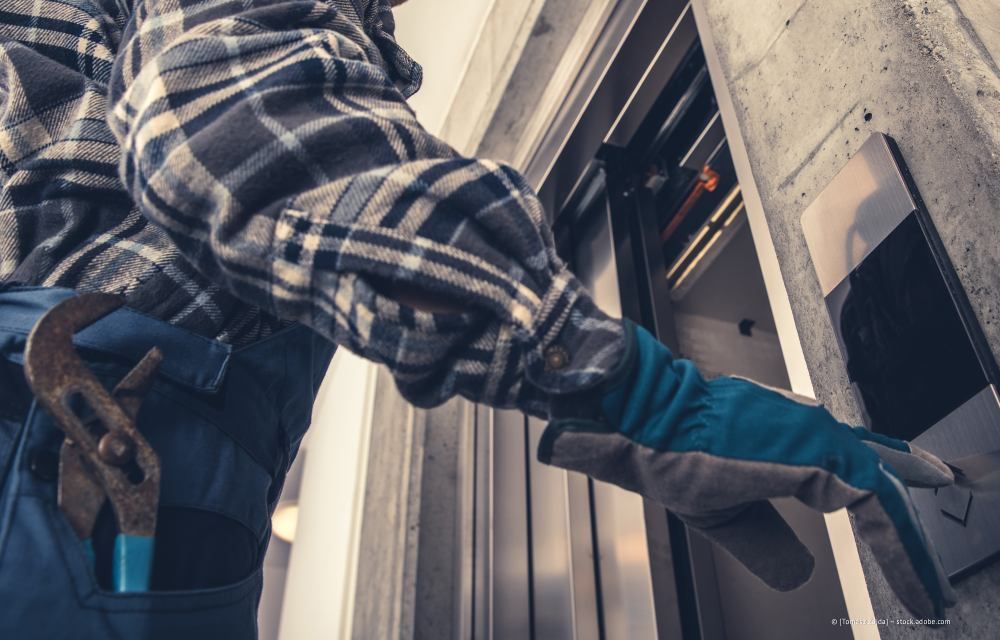 Ein Arbeiter greift mit Werkzeuggürtel und Handschuhen durch einen Fensterrahmen, um eine Gebäudeaußenfassade zu montieren oder zu reparieren.