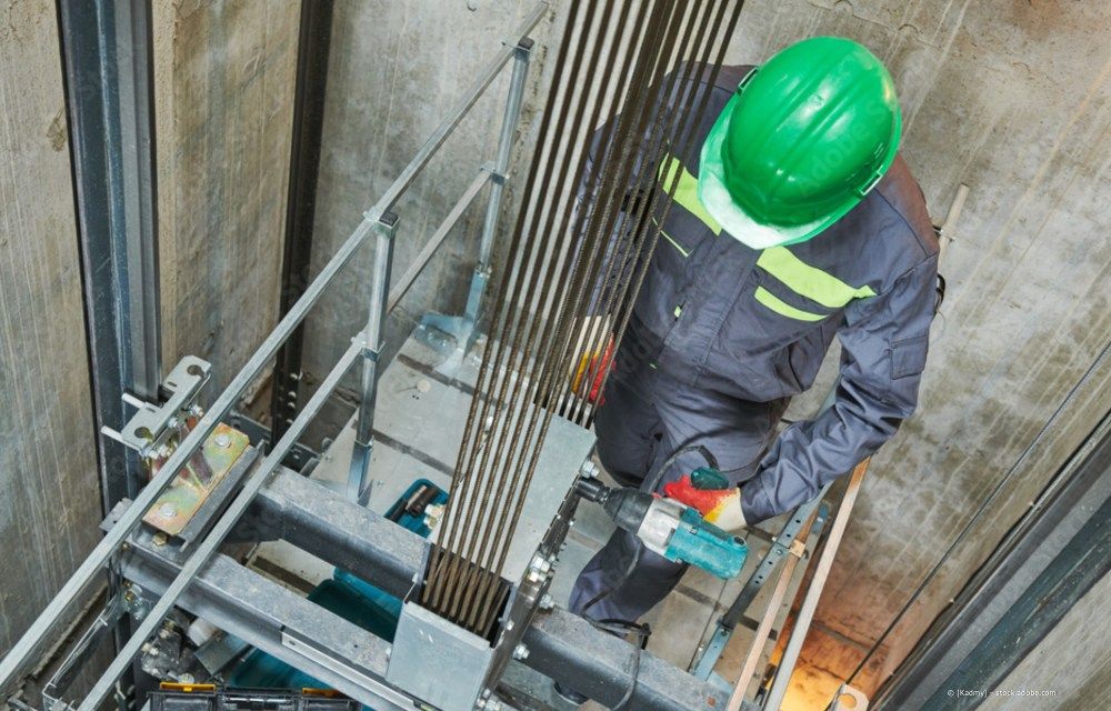 Arbeiter mit grünem Schutzhelm benutzt ein Werkzeug in einem Betonschacht mit Metallgerüst.