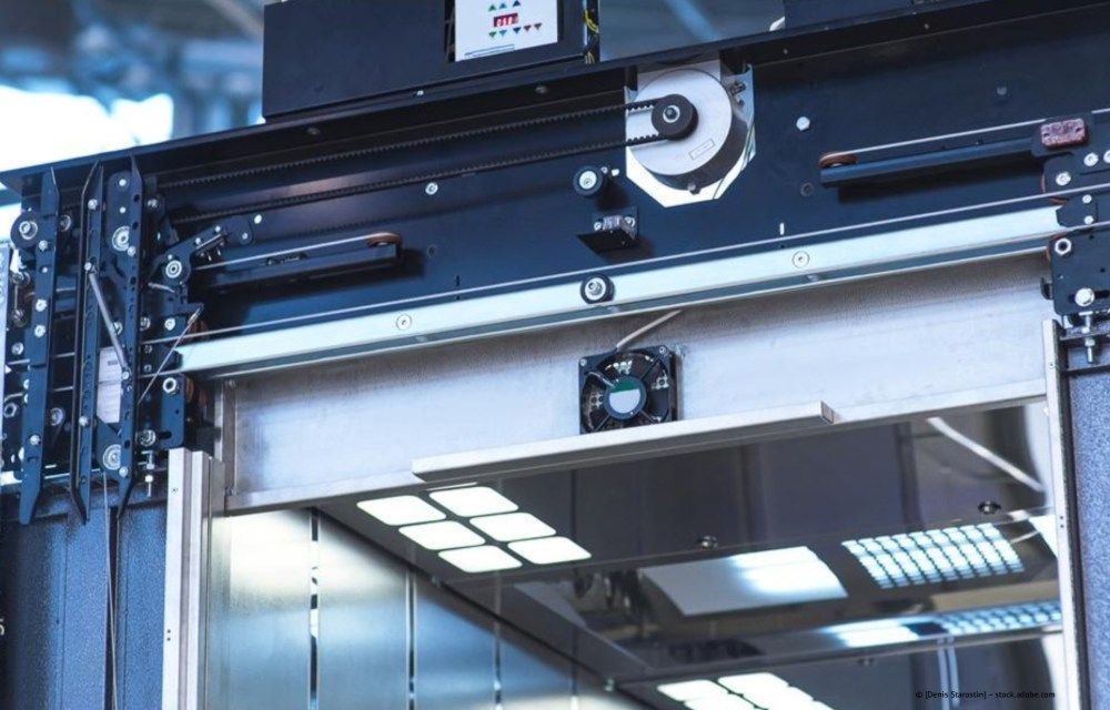Industrieller Garagentormechanismus mit schwarzen Schienen und silbernen Paneelen über einem reflektierenden Türrahmen